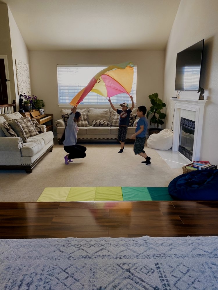 Children playing with a rainbow parachute in the living room